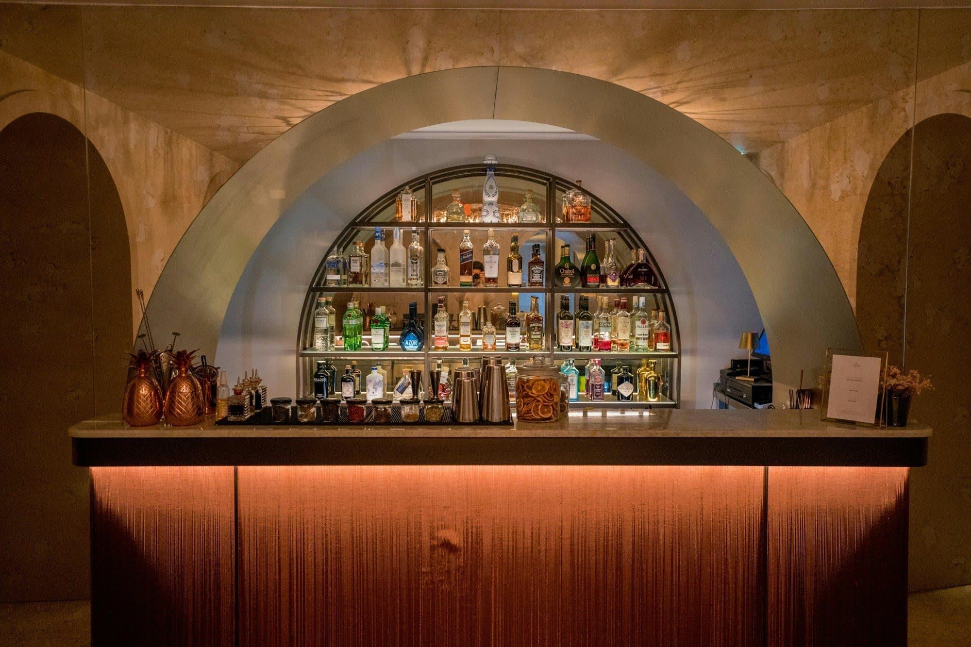 A backlit bar with shelves of bottles under an arch